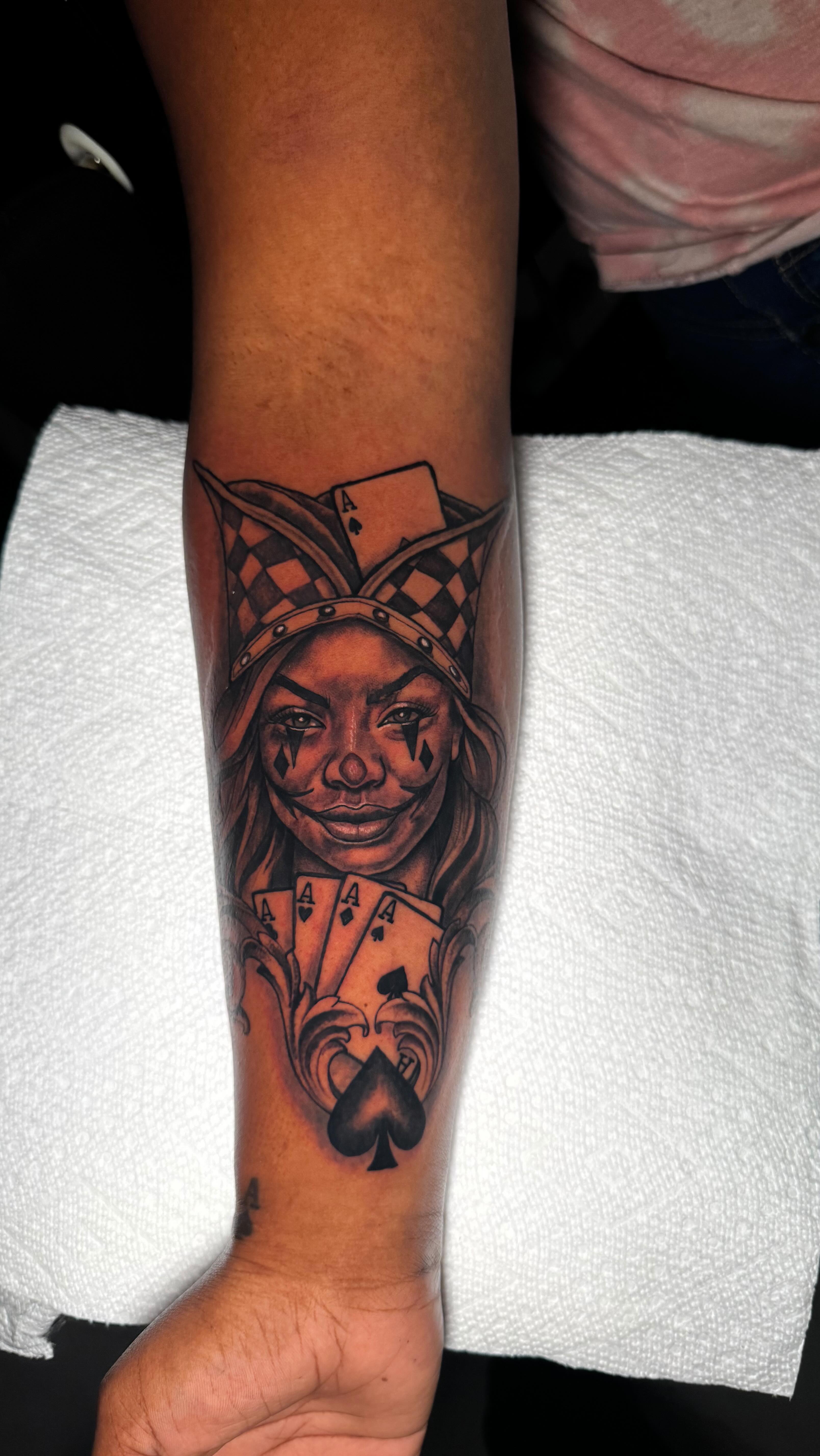 Black and grey realism jester portrait forearm tattoo