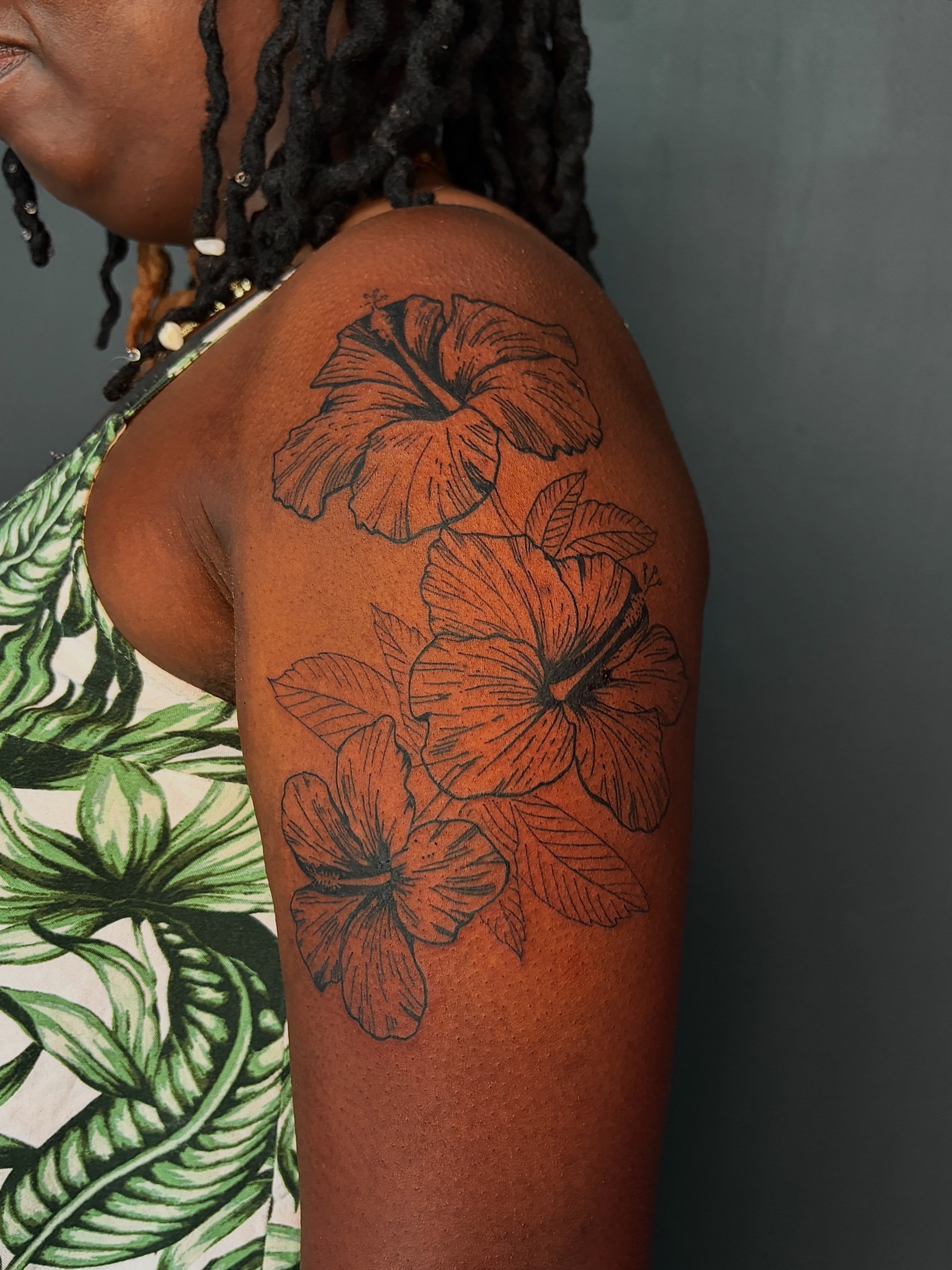 Fine line black hibiscus floral upper arm tattoo