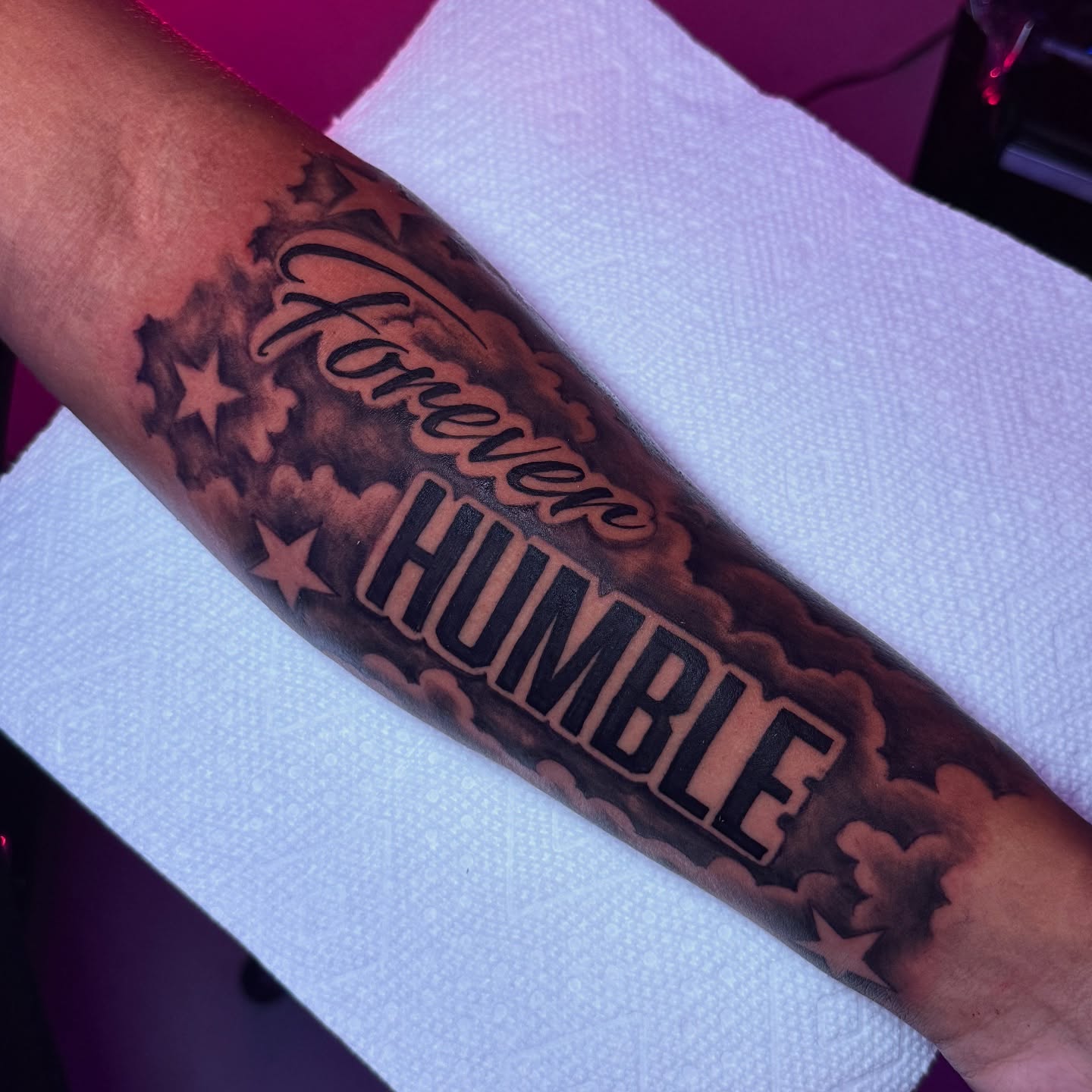 Black and grey lettering and clouds forearm tattoo